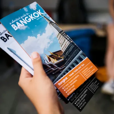 a picture of a hand holding 2 different brochures about Bangkok